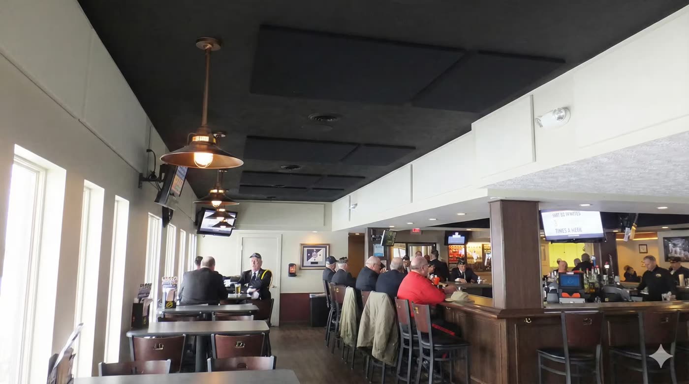 Bar/kafe tarzi mekanda tavana monte siyah akustik panel serisi, pencere kenari oturma alani, arka planda kucuk ve secilmeyen musteri siluetleri
