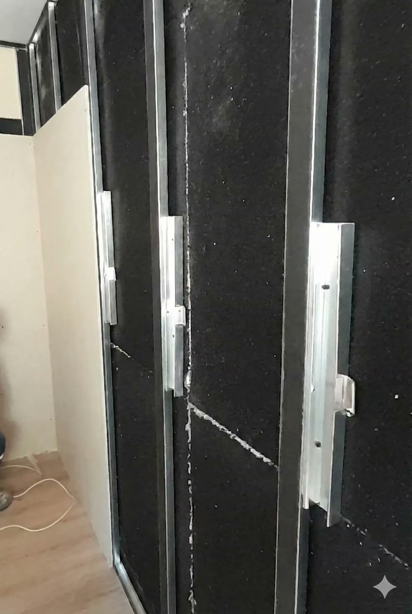 Duvara monte edilmiş siyah dokulu ses yalıtım panelleri, metal profil derzli, yakın çekim kurulum fotoğrafı