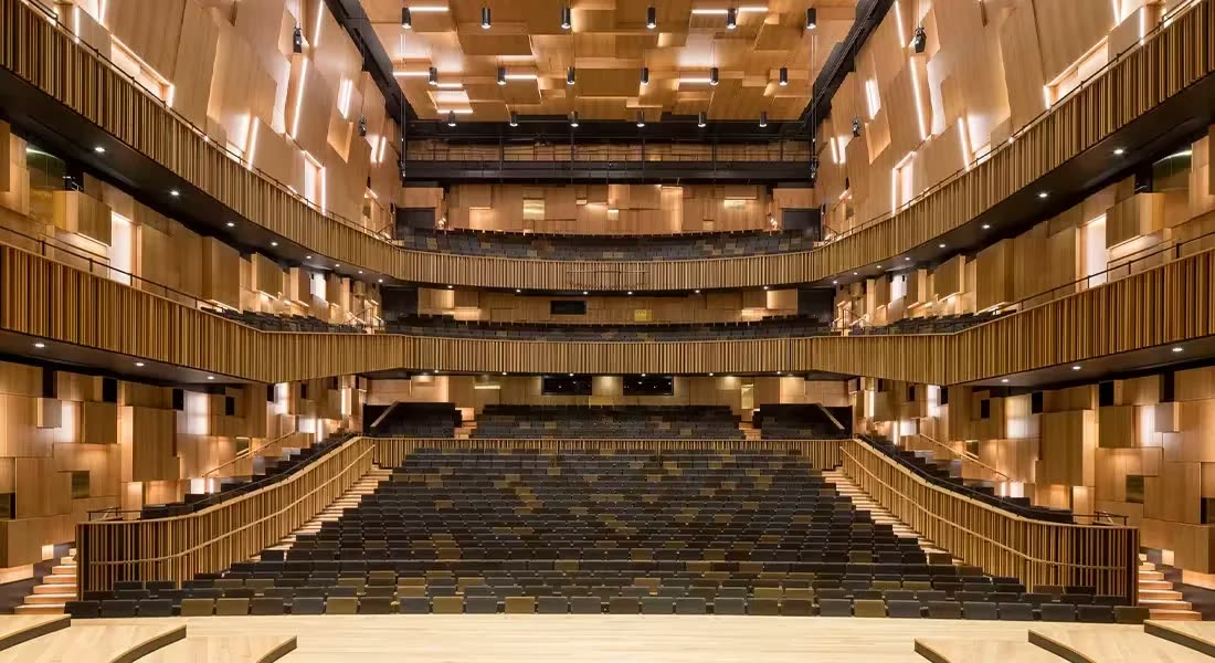 Çok katlı konser/tiyatro salonu iç mekanı; duvarlarda ahşap kütle/blok desenli difüzör panelleri, balkonlar ve koltuk sıraları açıkça görünüyor