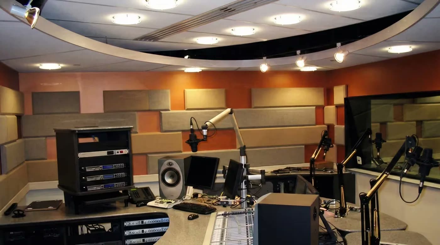 Radyo yayın stüdyosu: duvarlarda akustik paneller, mikrofon kolları, mikser masası, tavanda akustik düzenleme